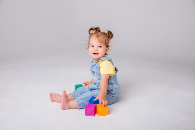 Une petite fille est assise sur un fond blanc et joue avec des cubes colorés des cubes de jouets pour enfants