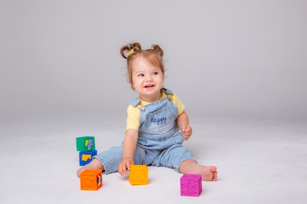 petite fille est assise sur un fond blanc et joue avec des cubes colorés. jouet pour enfant