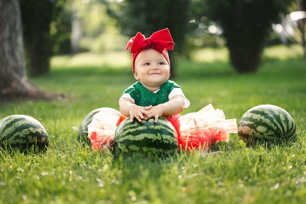 Petite fille est assise sur l'herbe verte dans une jupe en tulle rouge avec des pastèques