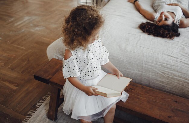 Une petite fille est assise avec un livre dans les mains à côté de sa mère. lire des livres pour enfants