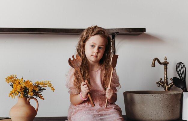 Une petite fille est assise sur la table de la cuisine avec des appareils de cuisson