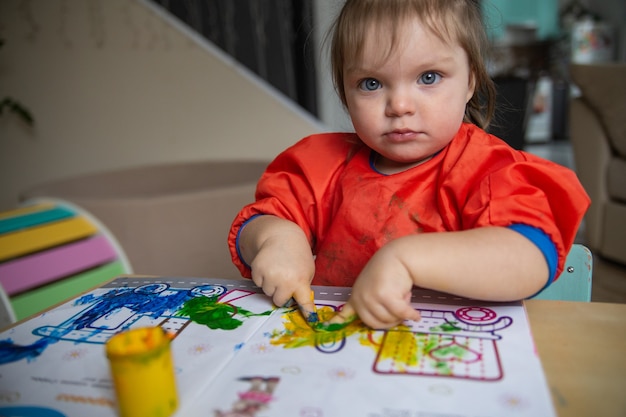 une petite fille est assise à une table et dessine avec des peintures au doigtLe concept de développement précoce