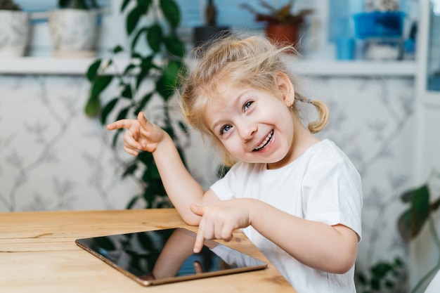 Une petite fille est assise à une table avec une tablette.