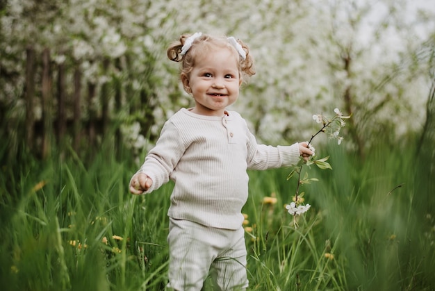 une petite fille est debout sur l'herbe. un enfant dans un jardin fleuri. une fille avec un sourire.