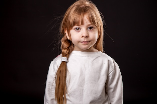 Une petite fille est gênée et coûte des yeux, un grand portrait en studio