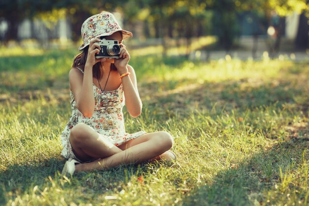 Petite fille est jouée par un appareil photo assis sur l'herbe dans le parc. Faire des selfies et photographier le monde autour