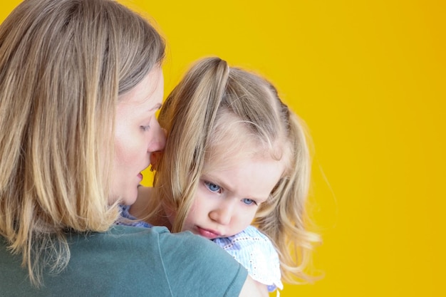 La petite fille est offensée bouleversée et s'assied dans les bras de sa mère Sur un fond jaune Maman calme sa fille