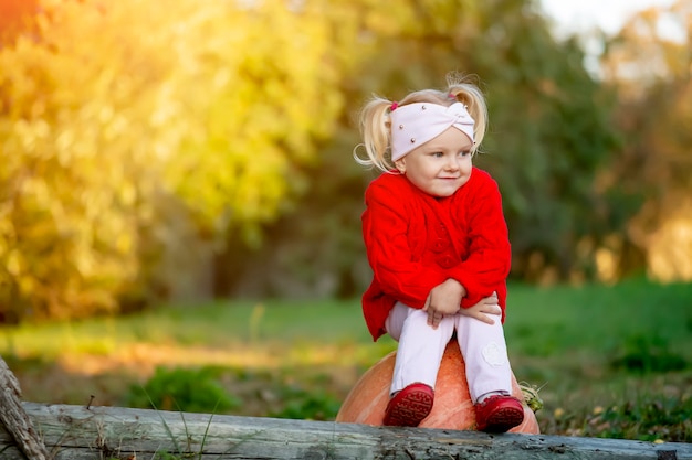 Petite fille est triste assis sur une citrouille dans le jardin d'automne