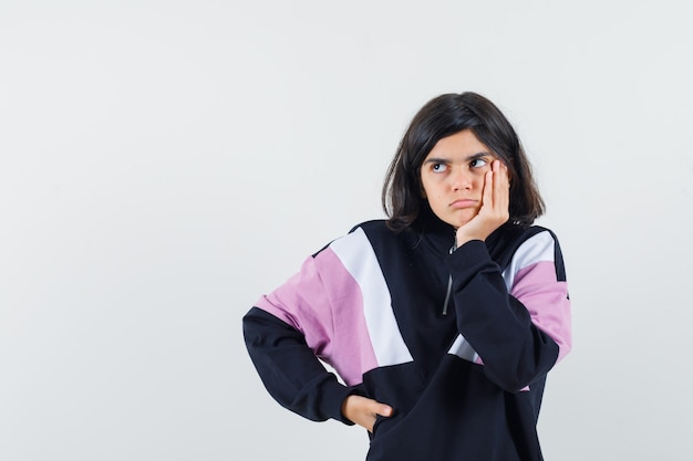 Petite fille étayant le menton sur place en chemise et à la pensif. vue de face.