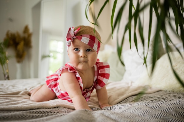 Une petite fille d'été en body avec un bandage sur la tête rampe sur le lit dans la chambre