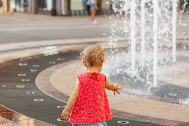 La petite fille étend ses mains à la fontaine brouillée