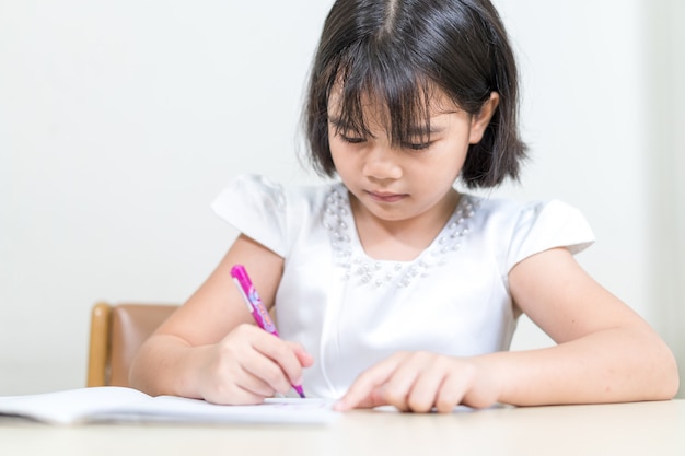 Petite fille étudiante écrivant sur un ordinateur portable à faire ses devoirs et à étudier soi-même à la maison