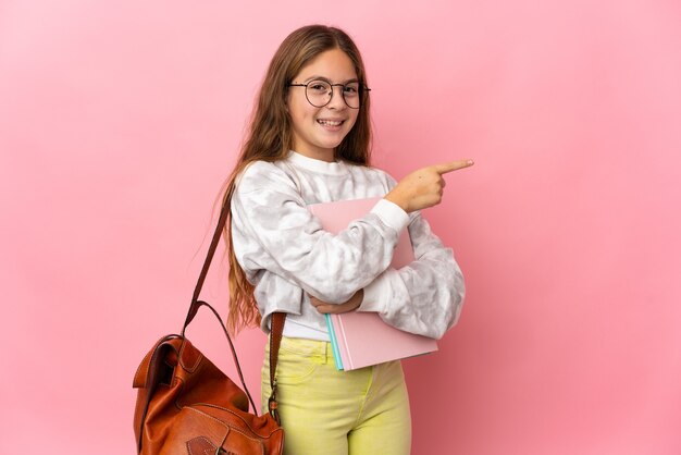 Petite fille étudiante sur fond rose isolé, pointant le doigt sur le côté