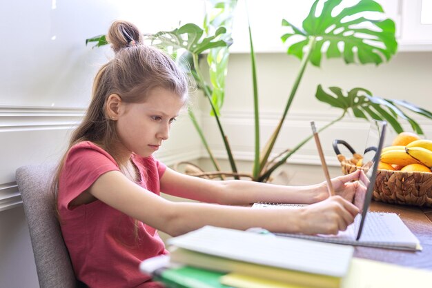 Petite fille étudie à la maison à l'aide d'une tablette numérique. Enseignement à distance, cours en ligne, visioconférence, cours scolaires sous forme électronique. École moderne, technologie, éducation, concept d'enfants.