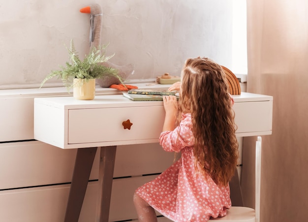 Une petite fille examine des livres sur une table dans une pièce