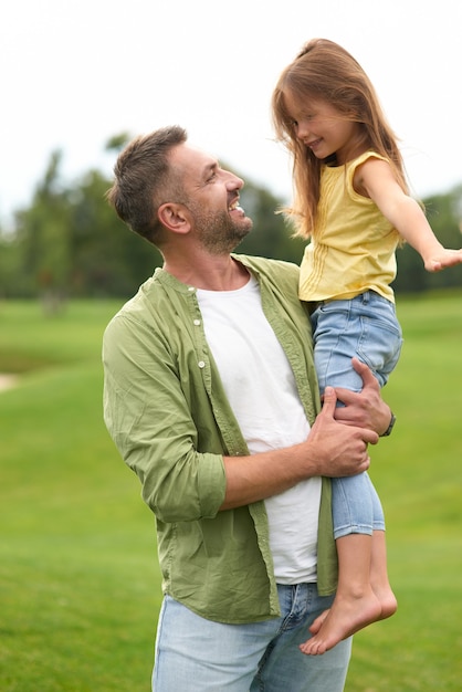 Petite fille excitée s'amusant avec son père pendant qu'il la tient et sa fille souriante et