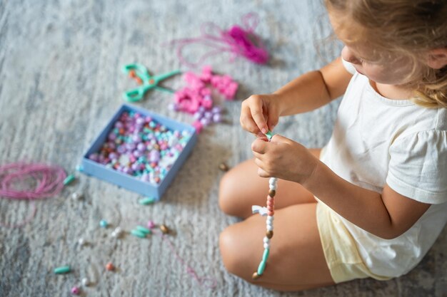 Petite fille fabriquant un bracelet de perles de bois à la maison salon La créativité des enfants et le développement de la motricité fine