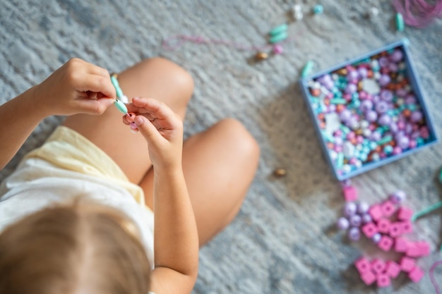 Petite fille faisant un bracelet de perles de bois à la maison dans le salon la créativité des enfants et le