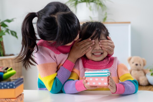 Petite fille faisant un cadeau à une petite fille heureuse tenant une boîte-cadeau, fermant les yeux d'un sourire mignon excité par la surprise d'anniversaire de sa sœur