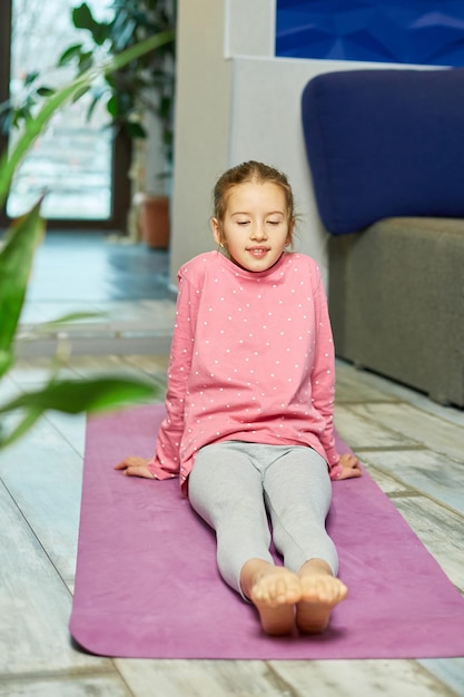 Petite fille faisant des exercices d'étirement, pratiquant le yoga sur un tapis de fitness à la maison