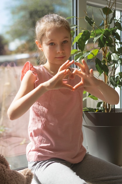Petite fille faisant un geste cardiaque avec ses doigts sur la fenêtre.