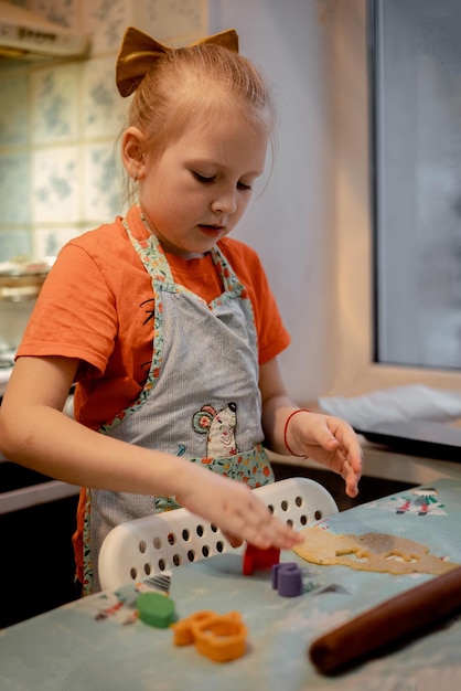 Une petite fille fait des biscuits à partir de pâte dans la cuisine
