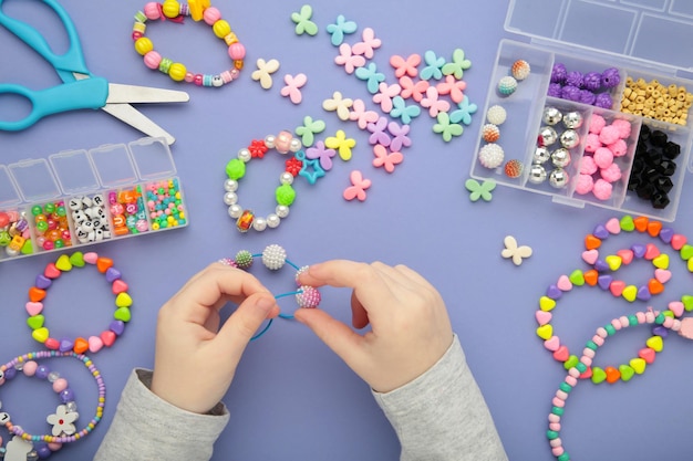 Photo une petite fille a fait des bracelets sur fond violet des enfants ont fait à la main des bijoux en perles