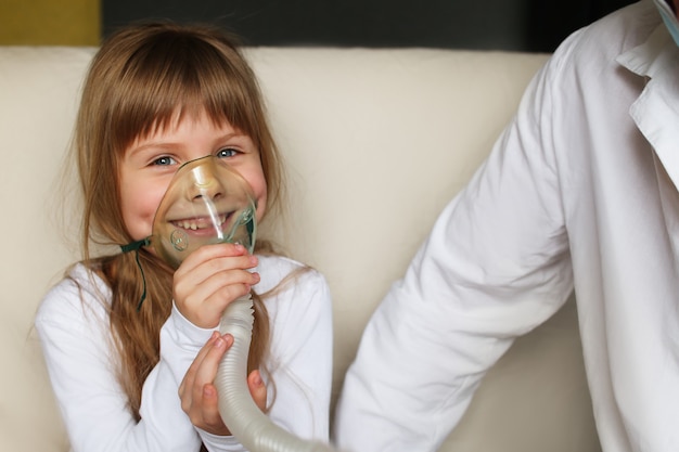 Une petite fille fait l'inhalation avec un spray à la maison, un médecin est à proximité. Inhalateur pour les enfants de l'asthme nébuliseur d'inhalation à vapeur concept de toux malade.