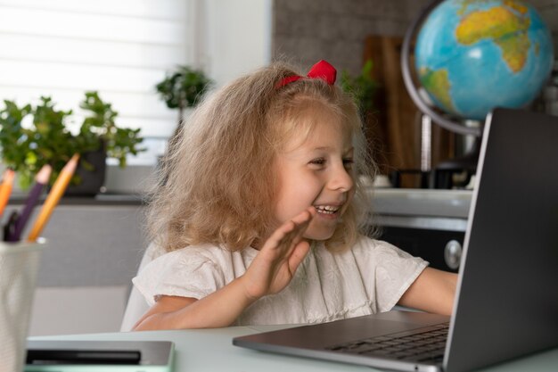 La petite fille fait des leçons à la maison à une communication vidéo de formation en ligne d'ordinateur portable