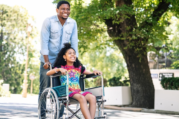 Une petite fille en fauteuil roulant appréciant et s'amusant avec son père lors d'une promenade ensemble à l'extérieur