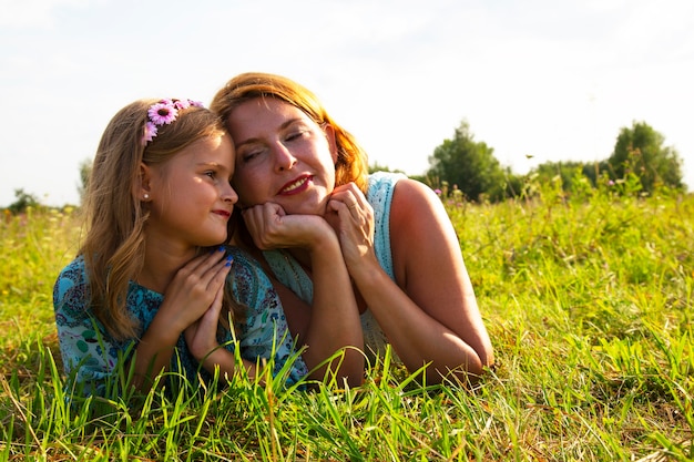 Une petite fille et une femme-mère sont allongées sur l'herbe verte dans un champ, un temps d'été ensoleillé, le sourire et la joie d'un enfant, une fille raconte les secrets de ses enfants