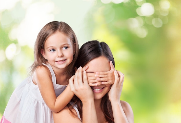 Petite fille fermant les yeux de sa mère avec les mains sur fond vert flou