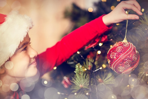 Petite fille festive accrochant une décoration de noël sur fond rougeoyant