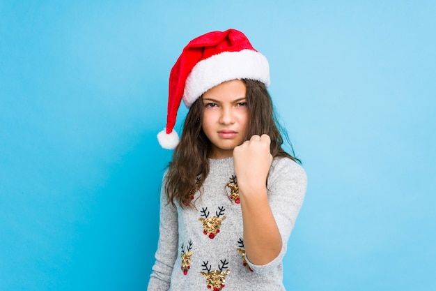 Petite fille fête le jour de Noël montrant le poing à la caméra, expression faciale agressive.