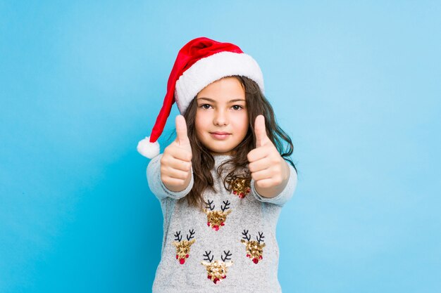 Petite fille fête le jour de Noël avec le pouce levé, acclamations à propos de quelque chose, soutien et concept de respect.