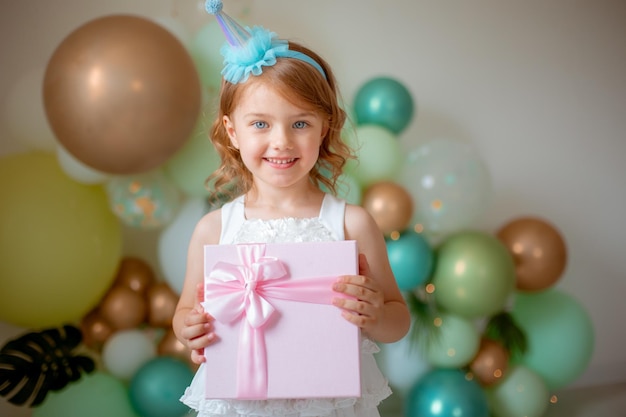 Une petite fille fête son anniversaire sur fond de ballons tenant un cadeau