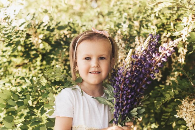 Petite fille avec des fleurs dans le champ Le bébé tient un bouquet de lupins dans ses mains Un enfant au milieu d'un champ recueille un bouquet de fleurs