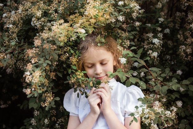 Petite fille avec des fleurs, portrait près de buisson en fleurs, gros plan. Le printemps. Concept de printemps.