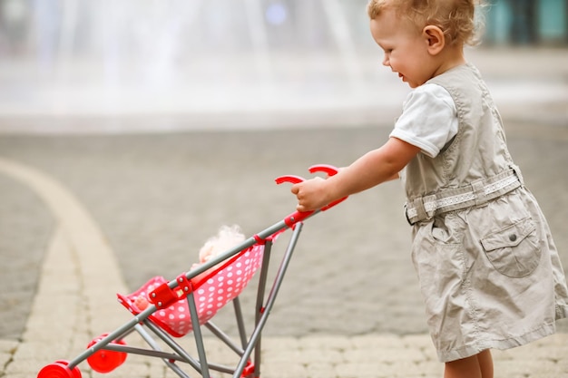 Petite fille floue poussant une petite poussette jouet contre une fontaine floue