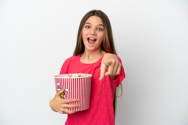 Petite fille sur fond blanc isolé tenant un gros seau de pop-corn tout en pointant vers l'avant