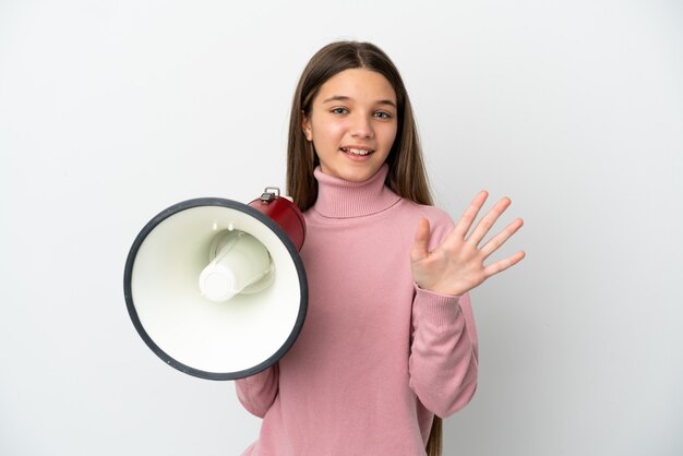 Petite fille sur fond blanc isolé tenant un mégaphone et saluant avec la main avec une expression heureuse