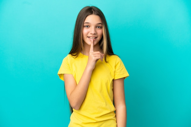 Petite fille sur fond bleu isolé montrant un signe de silence geste mettant le doigt dans la bouche