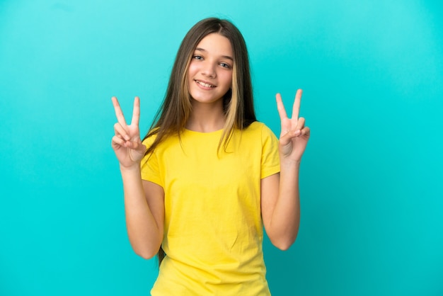 Petite fille sur fond bleu isolé montrant le signe de la victoire avec les deux mains