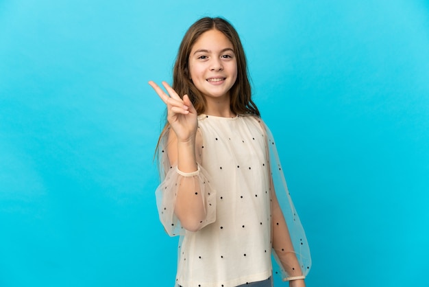 Petite fille sur fond bleu isolé souriant et montrant le signe de la victoire