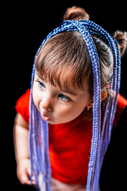 Une petite fille sur fond noir avec des tresses afro, tressées artificielles en bandes élastiques et mise sur mignon