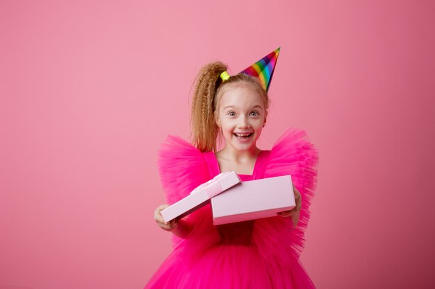 Une petite fille sur fond rose ouvre un cadeau célébrant son anniversaire