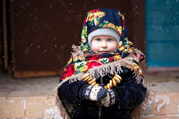 Une petite fille avec un foulard russe et des bagels à la fête de Maslenitsa