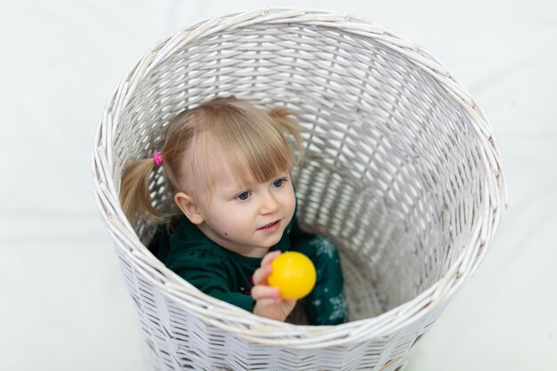 Une petite fille avec des franges courtes est assise dans un grand panier en osier et joue