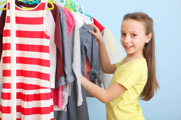 La petite fille gaie mignonne choisit des vêtements avec des cintres de plancher