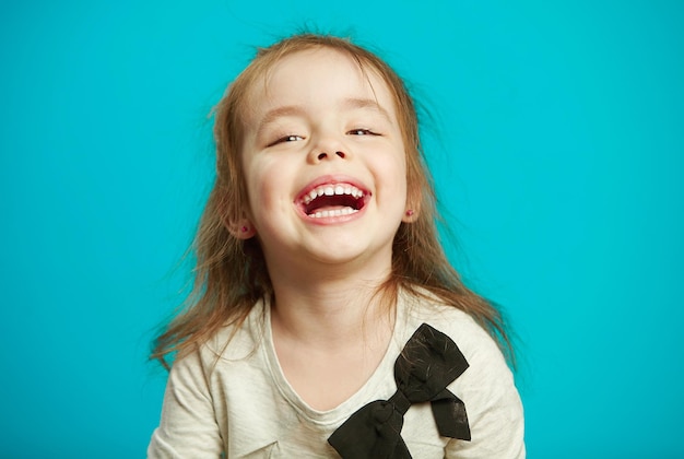 La petite fille gaie rit sur le fond bleu